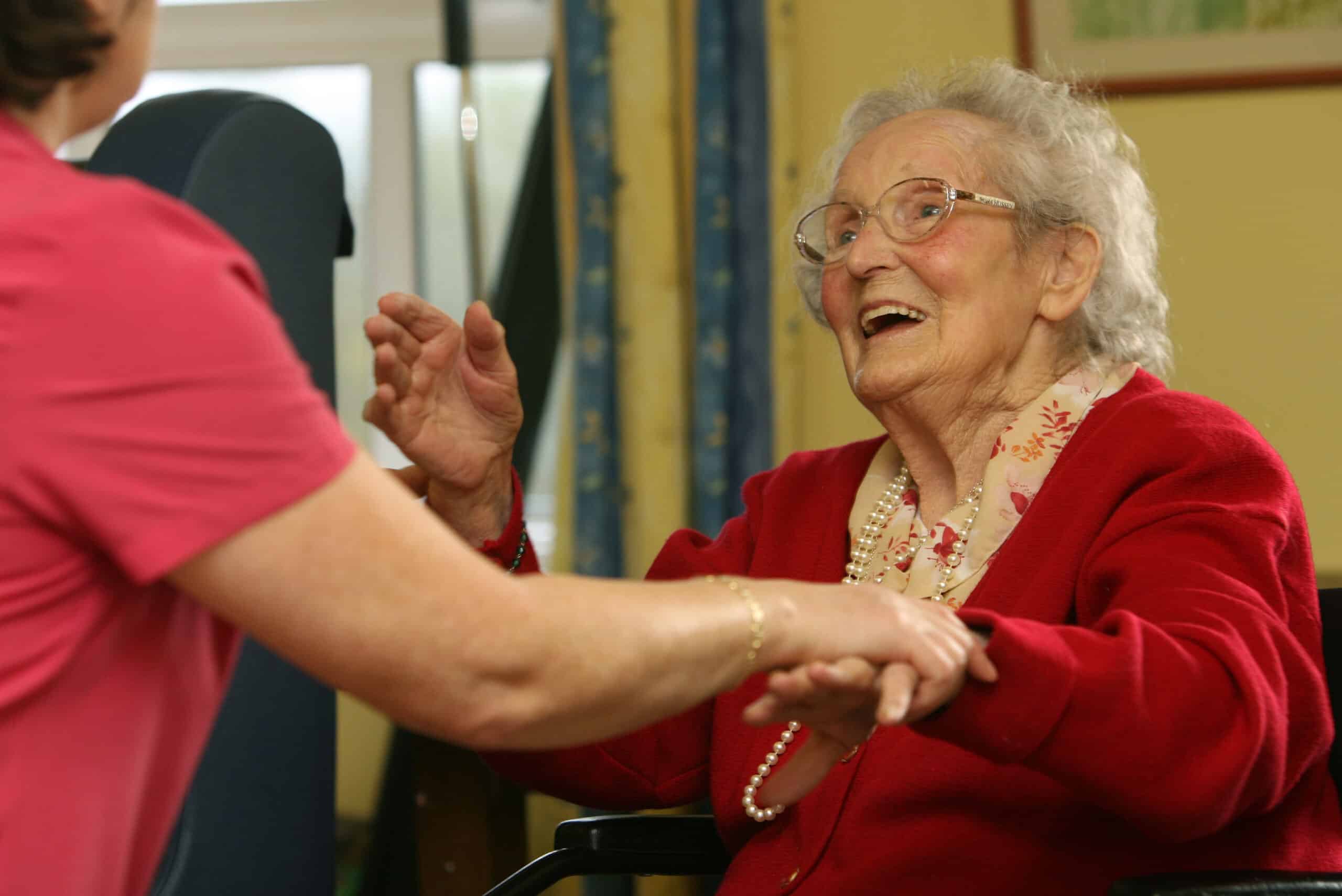 An elderly woman in a wheelchair shakes hands with a standing woman
