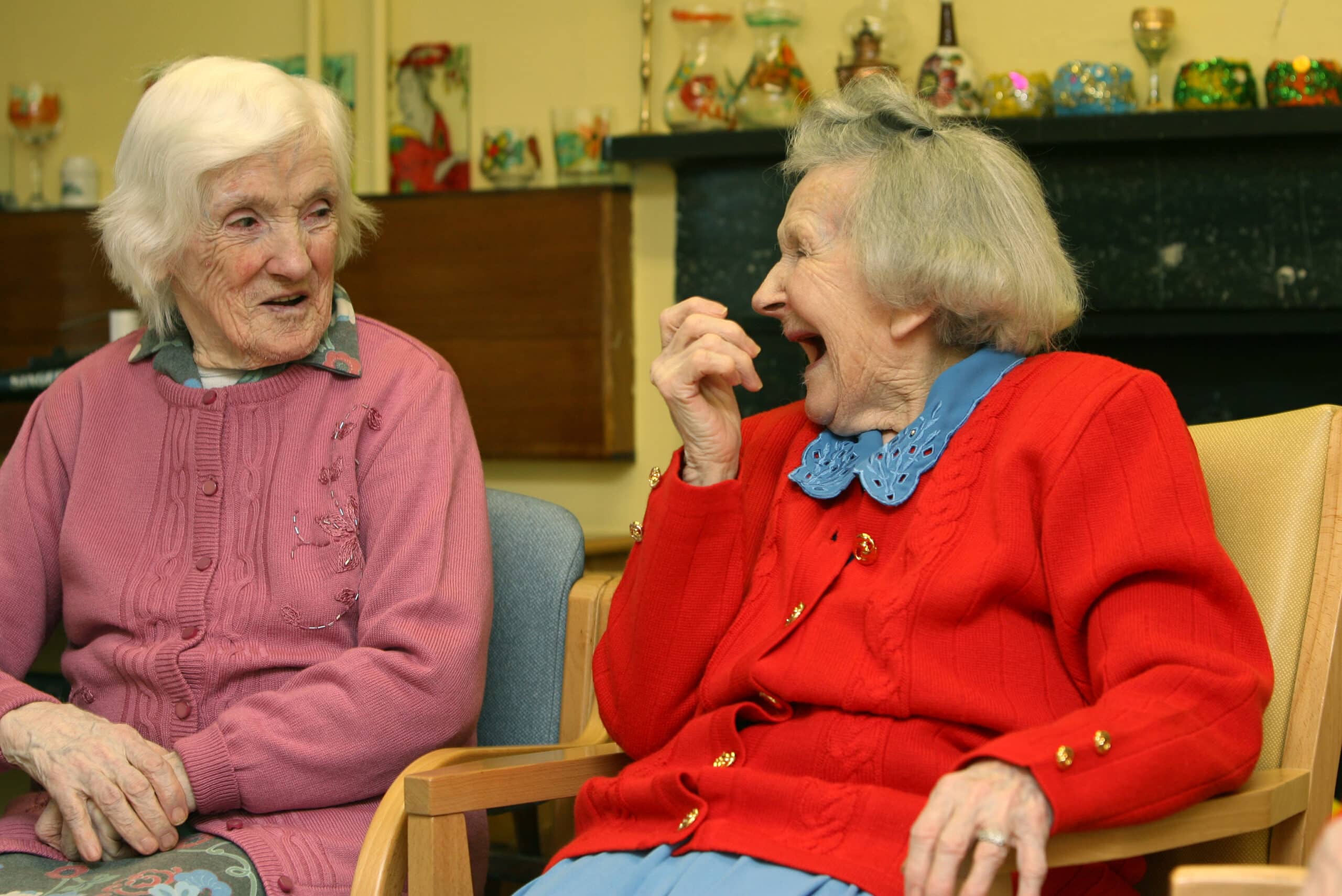Two elderly women sitting together in a chair, sharing a moment of conversation and companionship.