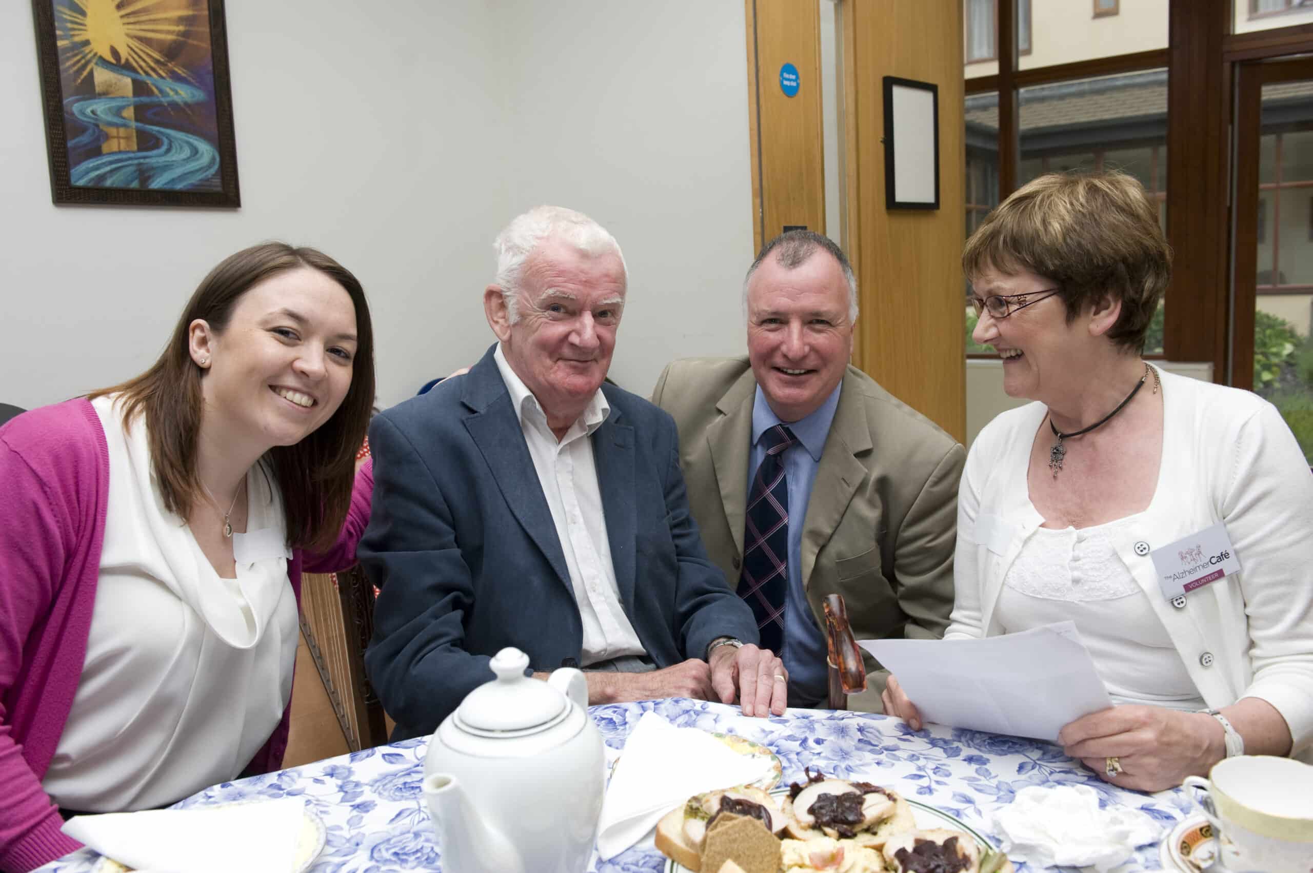 Three people enjoying tea together at a table, engaged in conversation and laughter.