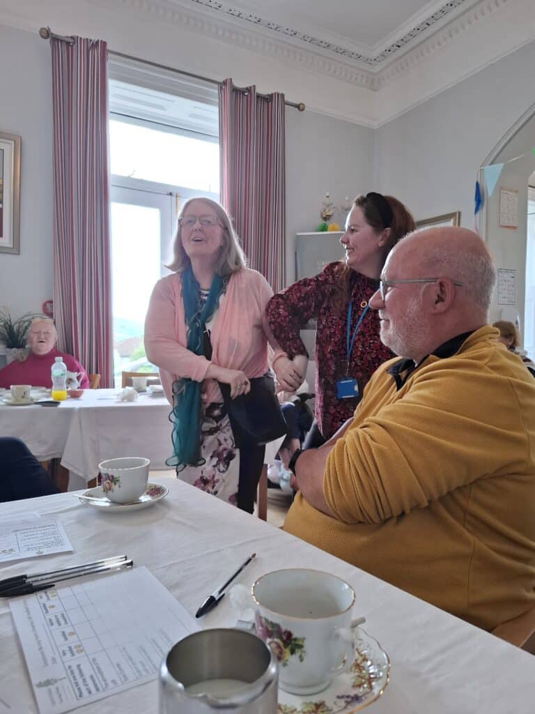 woman and two men enjoy tea together at a table, engaged in conversation and laughter.