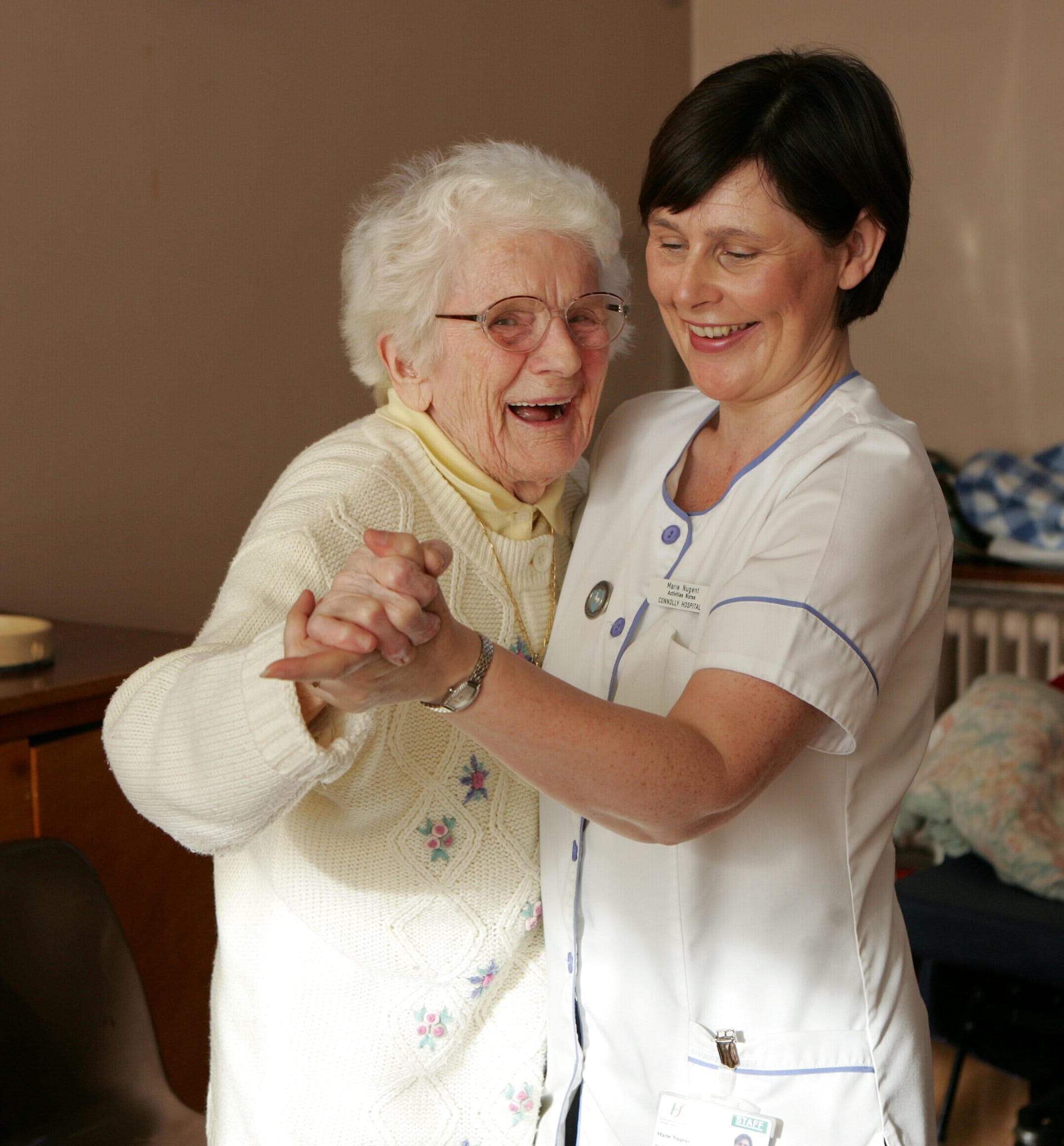 A nurse in uniform joyfully dances with an older woman, showcasing a moment of connection and happiness.
